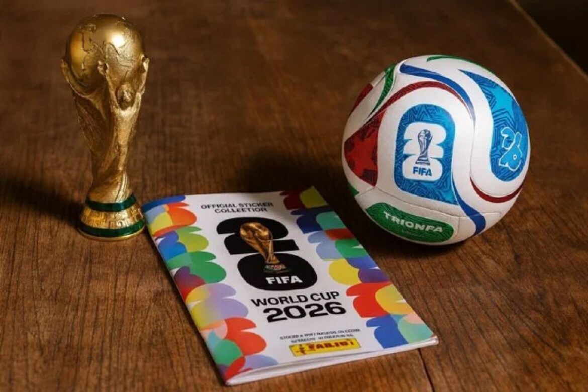 Troféu FIFA dourado, álbum Panini Copa 2026 colorido com logo 26 e bola Trionda azul com brasão FIFA sobre a mesa.