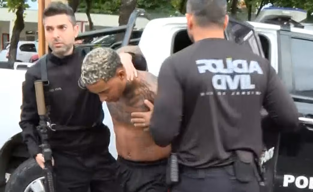 Prisão de MC Poze é mantida; entenda a decisão da Justiça 6 MC do Poze sem camisa com tatuagens no peito e cabelo descolorido, escoltado por dois agentes da Polícia Civil do Rio de Janeiro