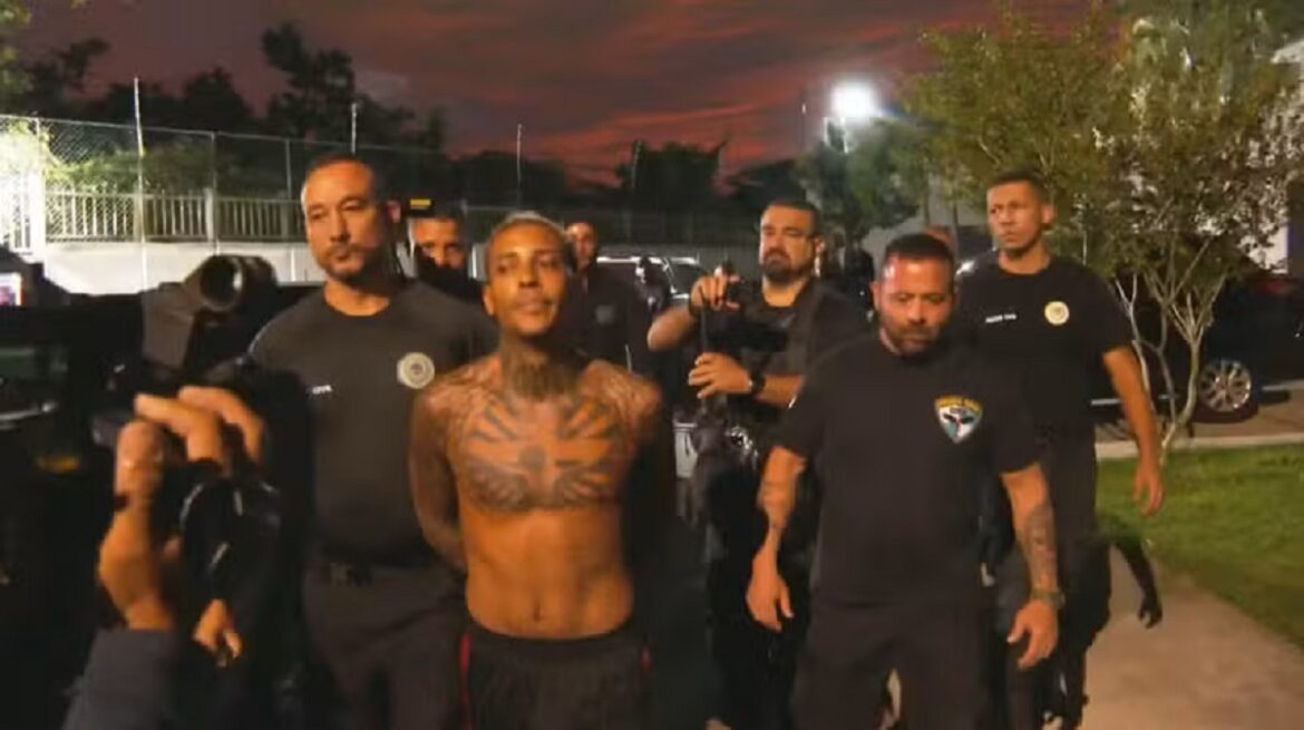 Funkeiro sem camisa, tatuagens no peito, é conduzido por agentes da PF em ambiente externo noturno com céu avermelhado