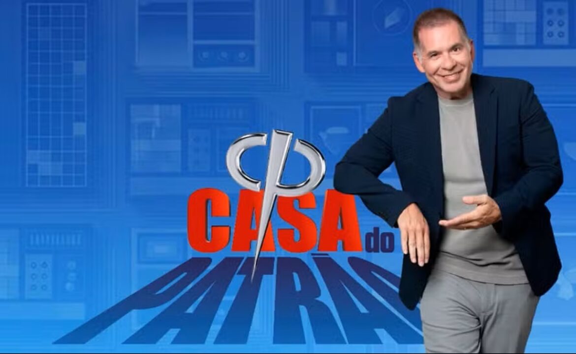 Leandro Hassum de blazer azul e camiseta cinza posa ao lado do logo Casa do Patrão sobre fundo azul