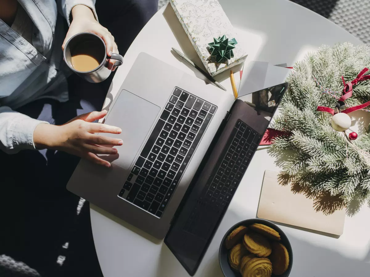 Trabalhar no feriado de 1º de maio: o que diz a lei sobre folgas e remuneração em 2026? 6 Mãos femininas segurando xícara de café e usando laptop em mesa branca com decorações natalinas