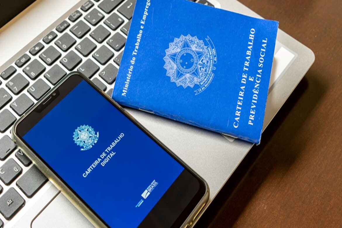 Carteira de Trabalho Digital em smartphone ao lado da CTPS física azul sobre teclado de notebook cinza