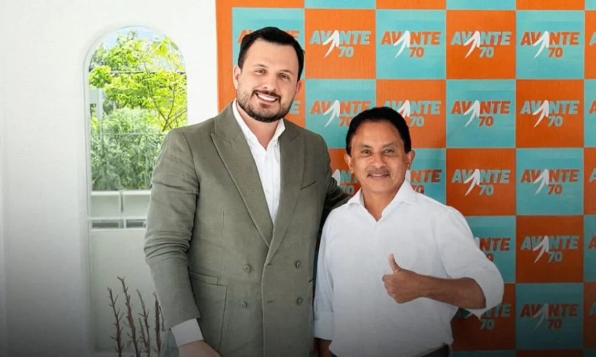 Cantor Manoel Gomes, do hit "Caneta Azul", posa sorrindo ao lado de político em frente a painel laranja e azul do partido Avante 70