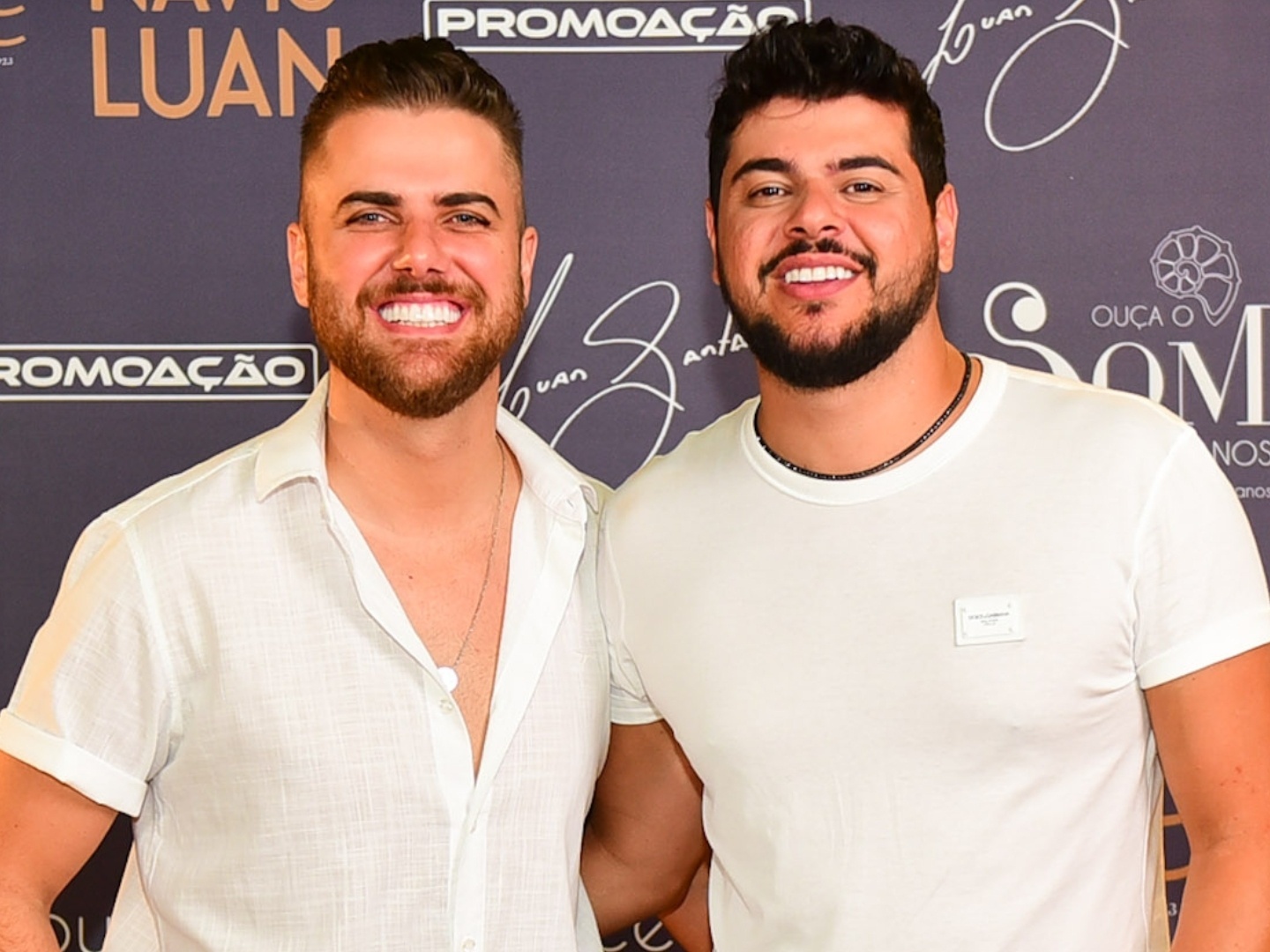 Música de Zé Neto e Cristiano associada a Vorcaro é proibida pela Justiça 6 Zé Neto e Cristiano sorrindo lado a lado em frente a painel promocional, ambos vestindo roupas claras
