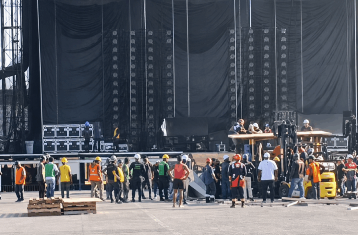 Operários e equipes de resgate reunidos em frente ao palco em montagem na Praia de Copacabana após acidente fatal com funcionário.