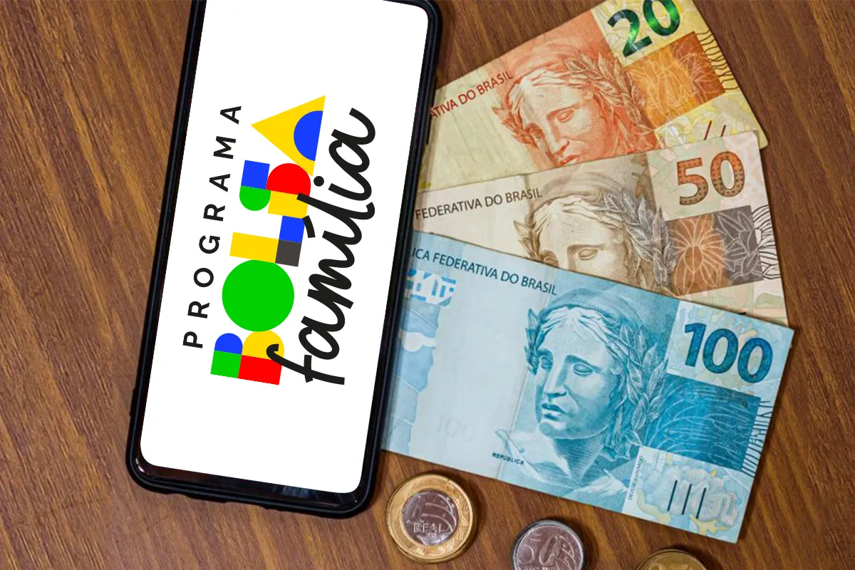 Últimas horas para público 1 do Bolsa Família atualizar dados e evitar bloqueio em maio 6 Celular exibindo aplicativo do Bolsa Família ao lado de cédulas de real e moedas sobre superfície de madeira.
