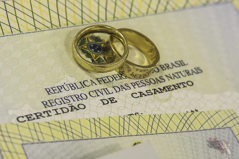 Mutirão oferece certidão de nascimento gratuita em todos os estados até 17 de abril 2 Par de alianças douradas sobrepostas a uma Certidão de Casamento brasileira, com destaque para o brasão da República e o texto