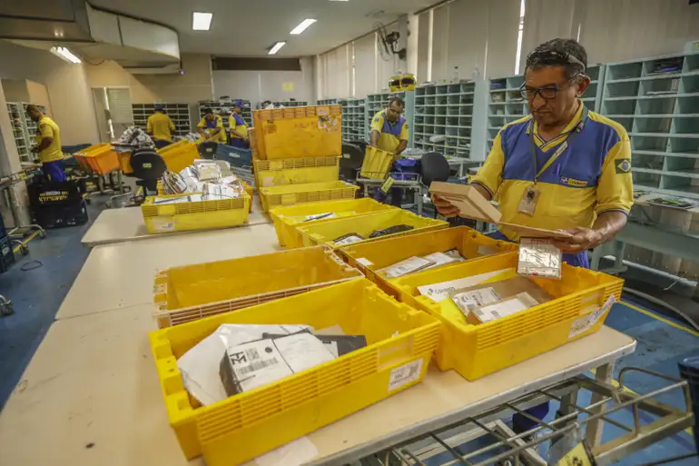 Correios reajustam preços de cartas e telegramas em 4,05%; encomendas ficam de fora 2 Funcionários dos Correios organizando pacotes em centro de distribuição.