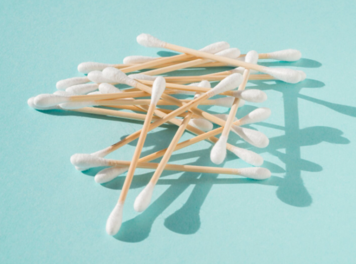 Pilha de cotonetes com hastes de madeira e pontas de algodão branco espalhados sobre um fundo azul claro com sombras projetadas.