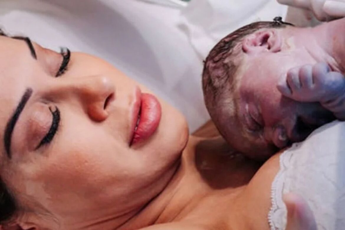 Close de Maíra Cardi com os olhos fechados, encostando o rosto em sua filha bebê logo após o nascimento. A bebê está com a cabeça apoiada no peito da mãe, em um momento de pele a pele. A imagem transmite cuidado, maternidade e proteção.