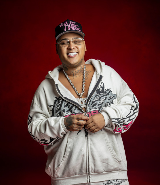 Justiça manda soltar MC Ryan, Poze do Rodo e proprietário da Choquei 6 Retrato de MC Ryan SP sorrindo, vestindo moletom branco com estampas pretas, boné preto e rosa, óculos de grau e exibindo grossas correntes e pingentes prateados sobre um fundo vermelho texturizado.