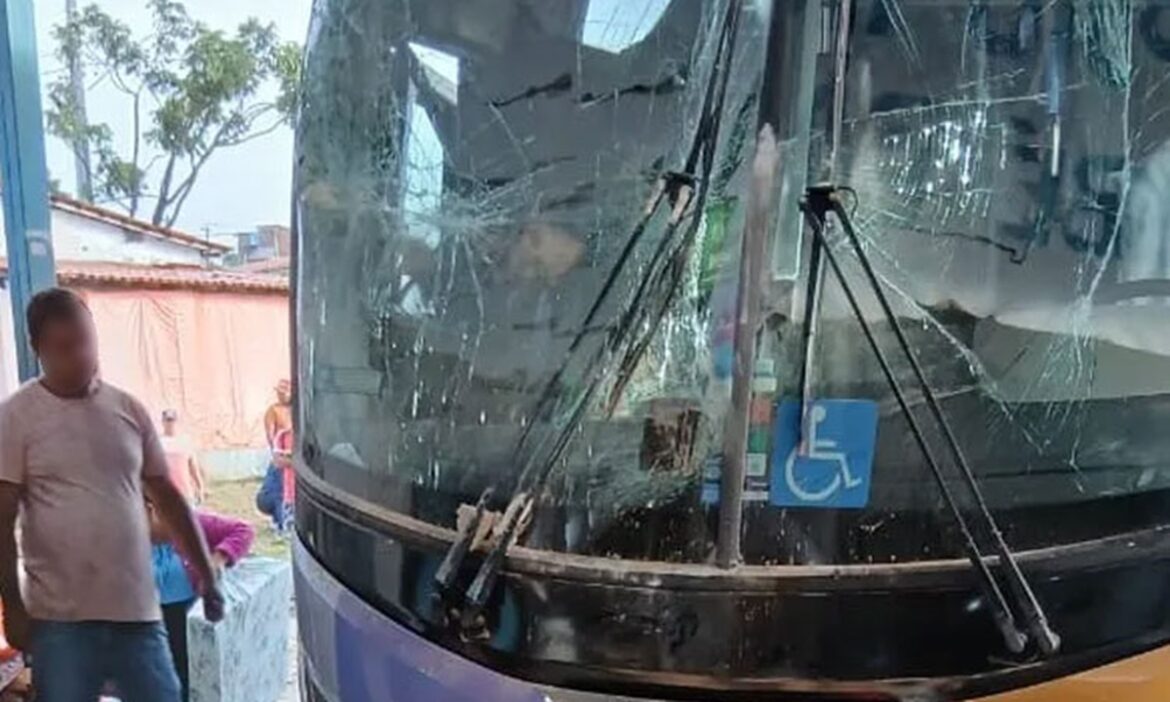 Ônibus com para-brisa estilhaçado e estrutura danificada após invadir ponto rodoviário em Itambé, Bahia, com homem ao lado.