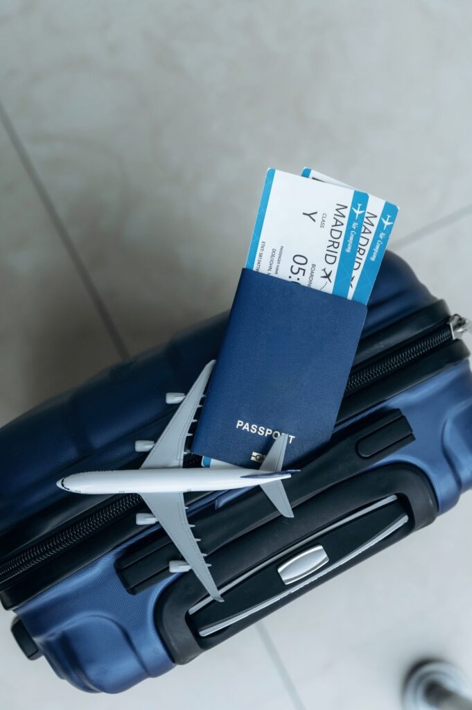 Quer achar passagem aérea fácil? Skyscanner lança ferramenta no ChatGPT com IA 6 Uma mala de viagem de cor azul escuro, rígida, vista de cima. Sobre ela, há um passaporte azul aberto com duas passagens aéreas (boarding passes) de Madrid inseridas. Ao lado, um modelo em miniatura de um avião comercial cinza. O fundo é um piso claro com linhas de rejunte.
