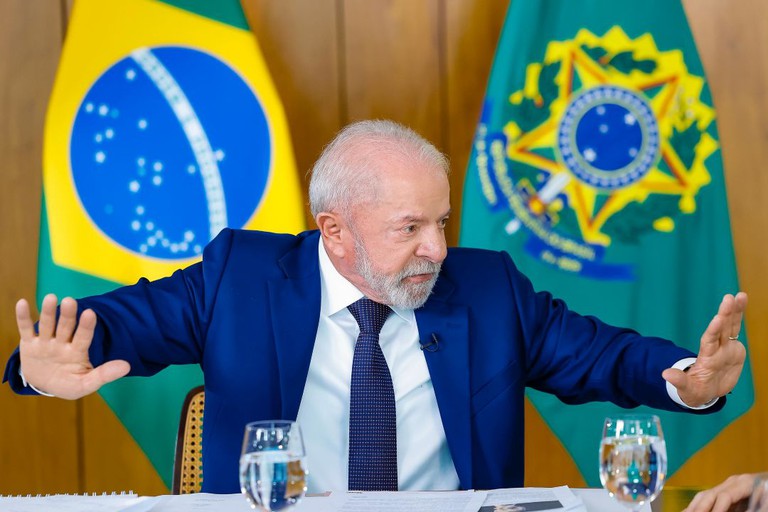 Escala 6x1 pode acabar, mas algumas profissões continuam de fora; saiba quais 6 O presidente Luiz Inácio Lula da Silva em reunião, gesticulando com as mãos à frente das bandeiras do Brasil e da Presidência, ilustrando o debate sobre a redução da jornada de trabalho e o fim da escala 6x1.