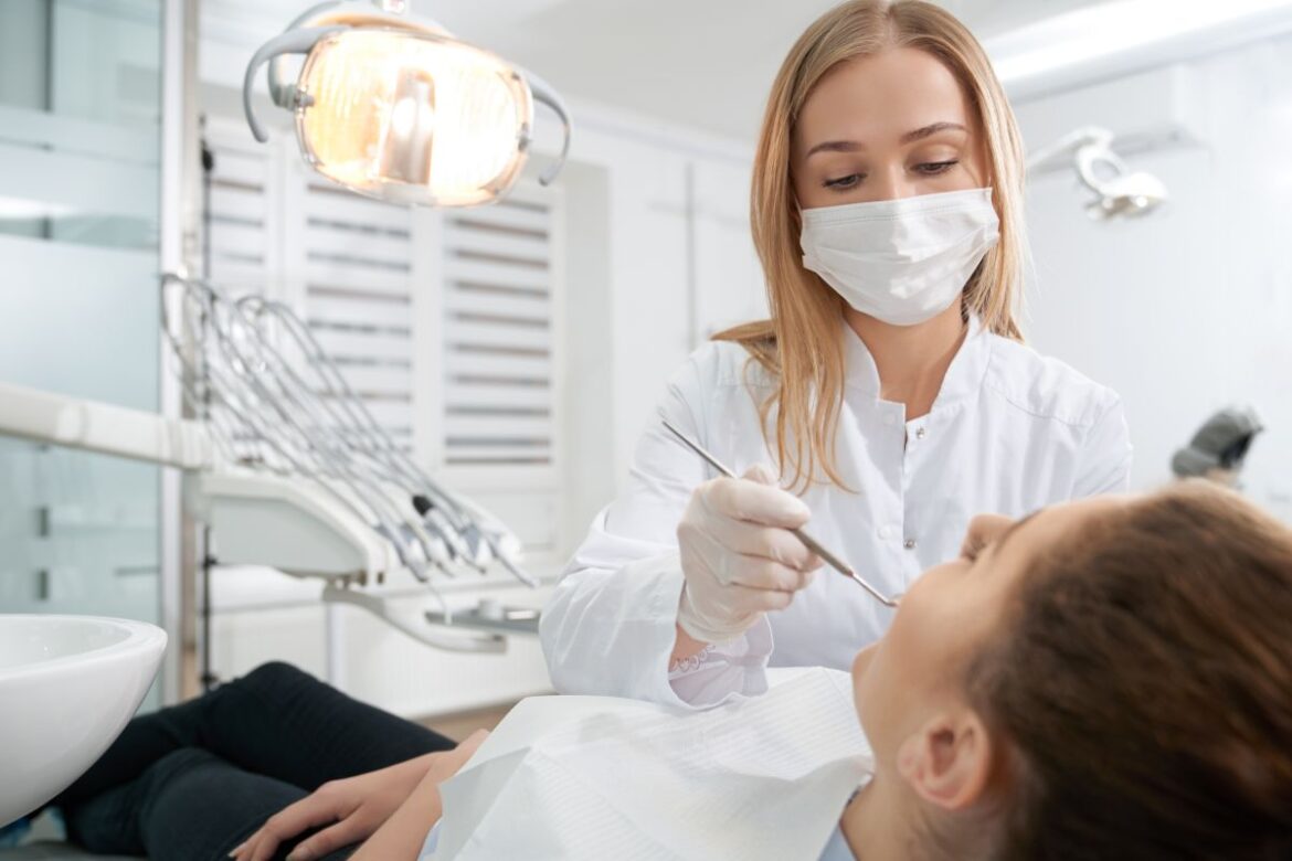 Dentista usando máscara e luvas atende paciente em consultório moderno, ilustrando o Programa de Reconstrução Dentária do SUS para mulheres vítimas de violência doméstica.