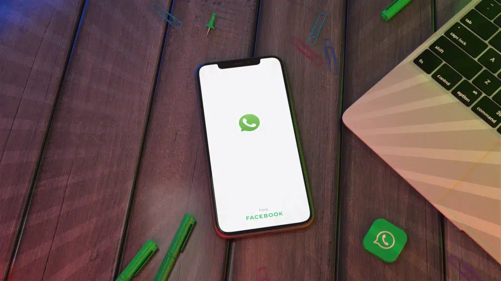 WhatsApp vai parar de funcionar em celulares Android antigos a partir de setembro; veja lista 6 Smartphone exibindo tela inicial do WhatsApp sobre mesa com notebook ao lado.