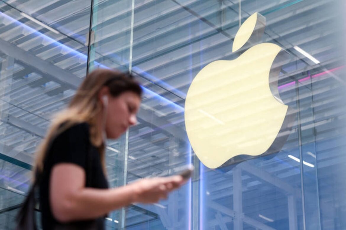 Mulher de camiseta preta com fones de ouvido usa iPhone diante da Apple Store com logo iluminado