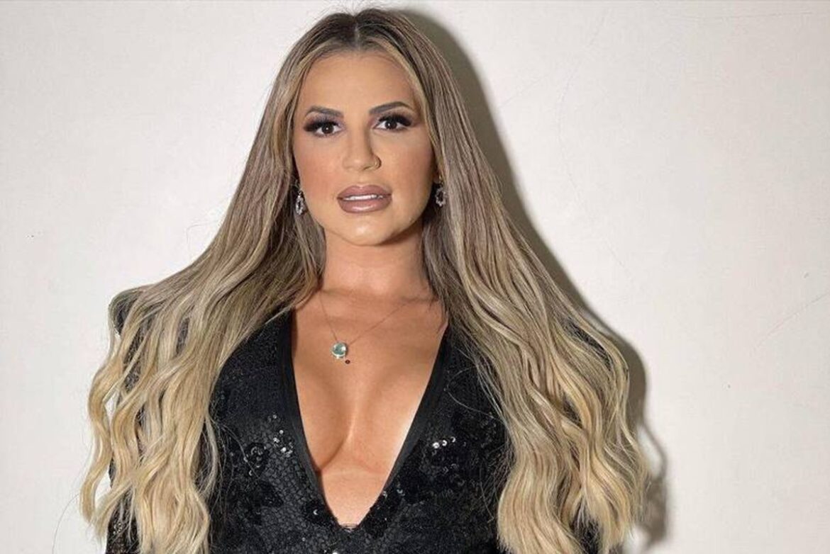 Deolane Bezerra com cabelos loiros longos, vestido preto decotado de paetês, brincos e colar delicado
