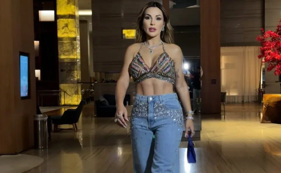 Deolane Bezerra é presa por suspeita de ligação com o PCC 6 Deolane Bezerra caminha em lobby de hotel usando top cropped brilhante e calça jeans com pedras, segurando bolsa azul