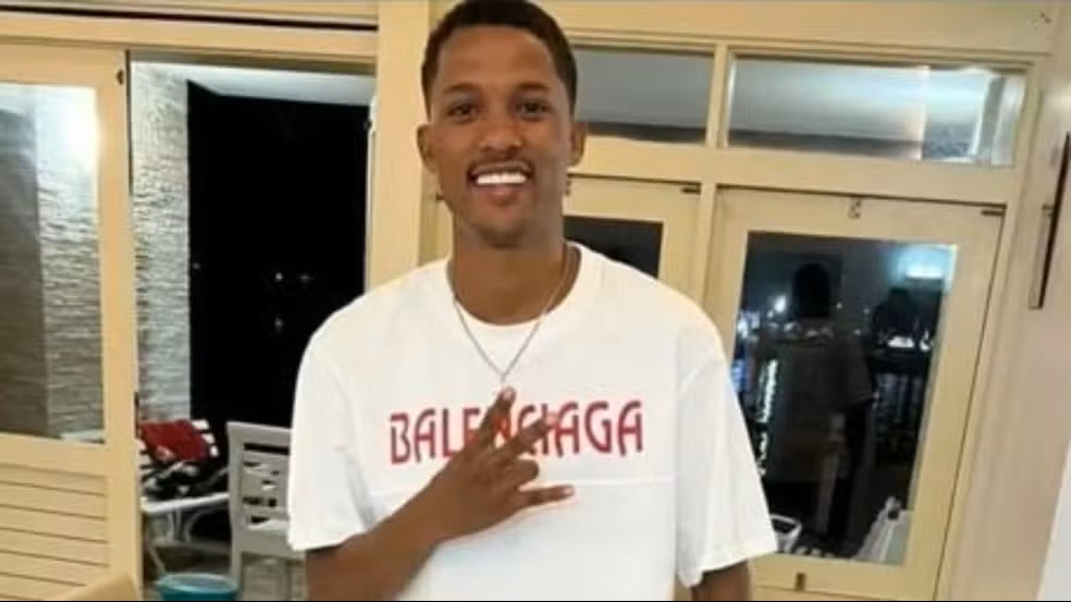 Ex-namorada assassinada: homem se entrega à polícia e história causa indignação nas redes sociais 6 Jovem negro sorridente com camiseta branca Balenciaga, colar de prata e mão sobre o peito em ambiente interno