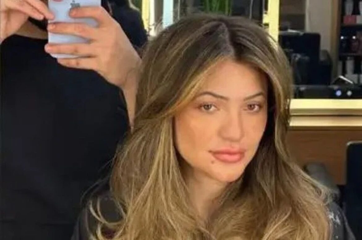 Mulher de cabelos loiros com mechas posa em salão de beleza enquanto profissional fotografa procedimento