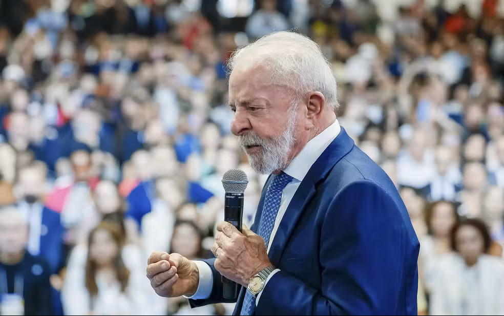 Adeus taxa das blusinhas! Governo Federal acaba de anunciar; veja o que muda 6 Presidente Lula segura microfone durante anúncio, usando terno azul e gravata, com plateia ao fundo