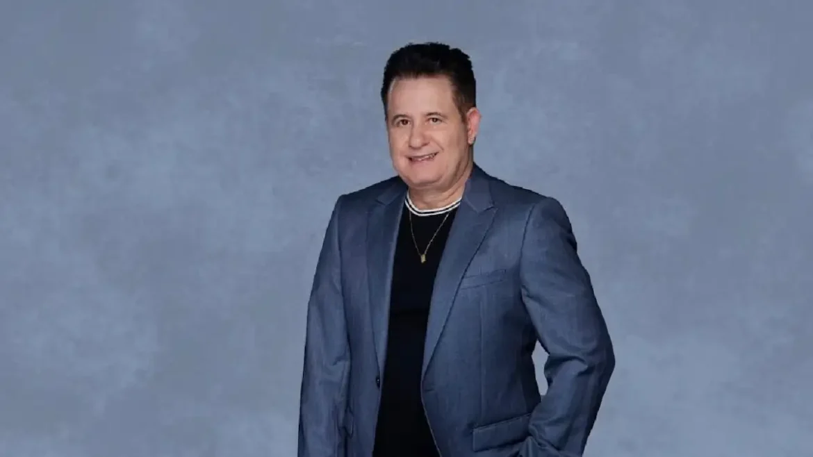 Cantor Marrone sorrindo, usando blazer cinza azulado e camiseta preta com colar dourado em fundo neutro