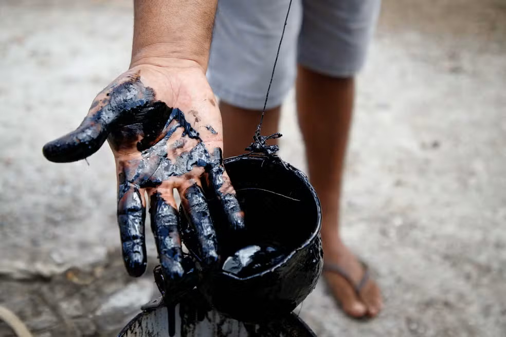 ANP confirma petróleo cru em sítio no Ceará após testes físico-químicos 6 Mão coberta de petróleo cru preto e viscoso segura balde cheio do líquido escuro em propriedade rural no Ceará