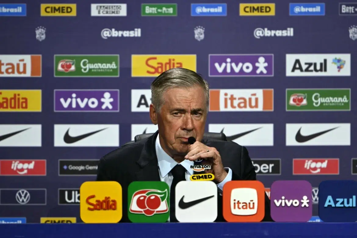 Técnico Carlo Ancelotti com microfone em coletiva de imprensa da CBF com painel de patrocinadores ao fundo