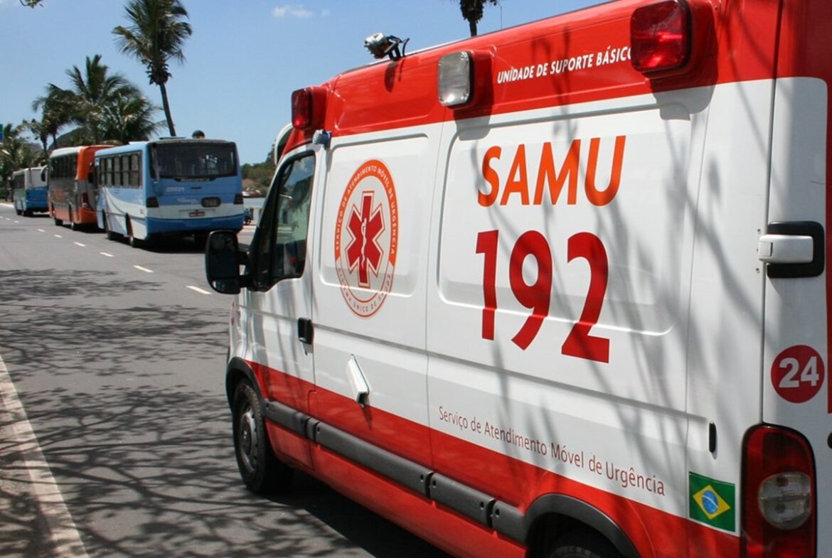Ambulância branca e vermelha do SAMU 192 estacionada em via pública, com símbolo da Estrela da Vida e bandeira do Brasil