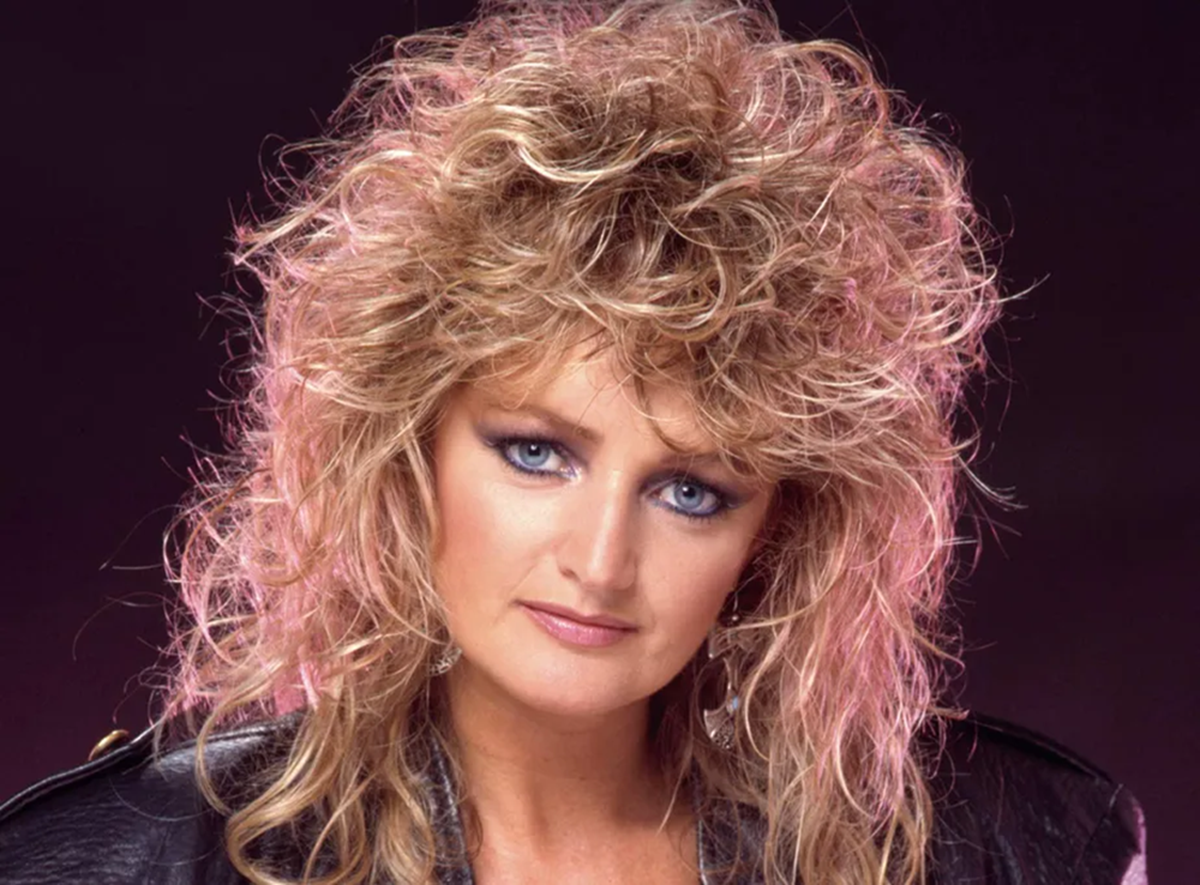 Bonnie Tyler entra em coma induzido após cirurgia de emergência 6 Bonnie Tyler com cabelos loiros volumosos e mechas rosas, jaqueta preta de couro e olhos azuis em estúdio fotográfico