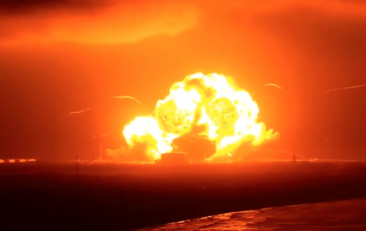 Nave da Blue Origin explode durante teste na plataforma de lançamento; nenhum funcionário se feriu 6 Grande bola de fogo da explosão de um foguete vista à distância, iluminando o céu alaranjado sobre a plataforma de lançamento