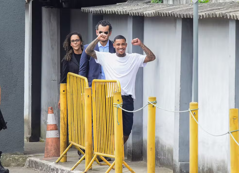 MC Poze do Rodo deixa a prisão após decisão da Justiça Federal 6 MC Poze do Rodo ergue os punhos comemorando ao deixar presídio, acompanhado de advogados, com grades amarelas à frente