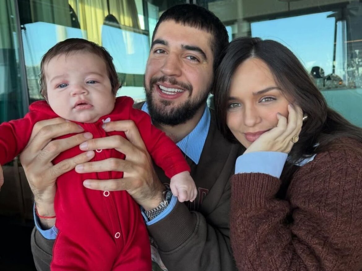 Rafa Kalimann e Nattan sorrindo com a filha Zuza de macacão vermelho no colo do pai