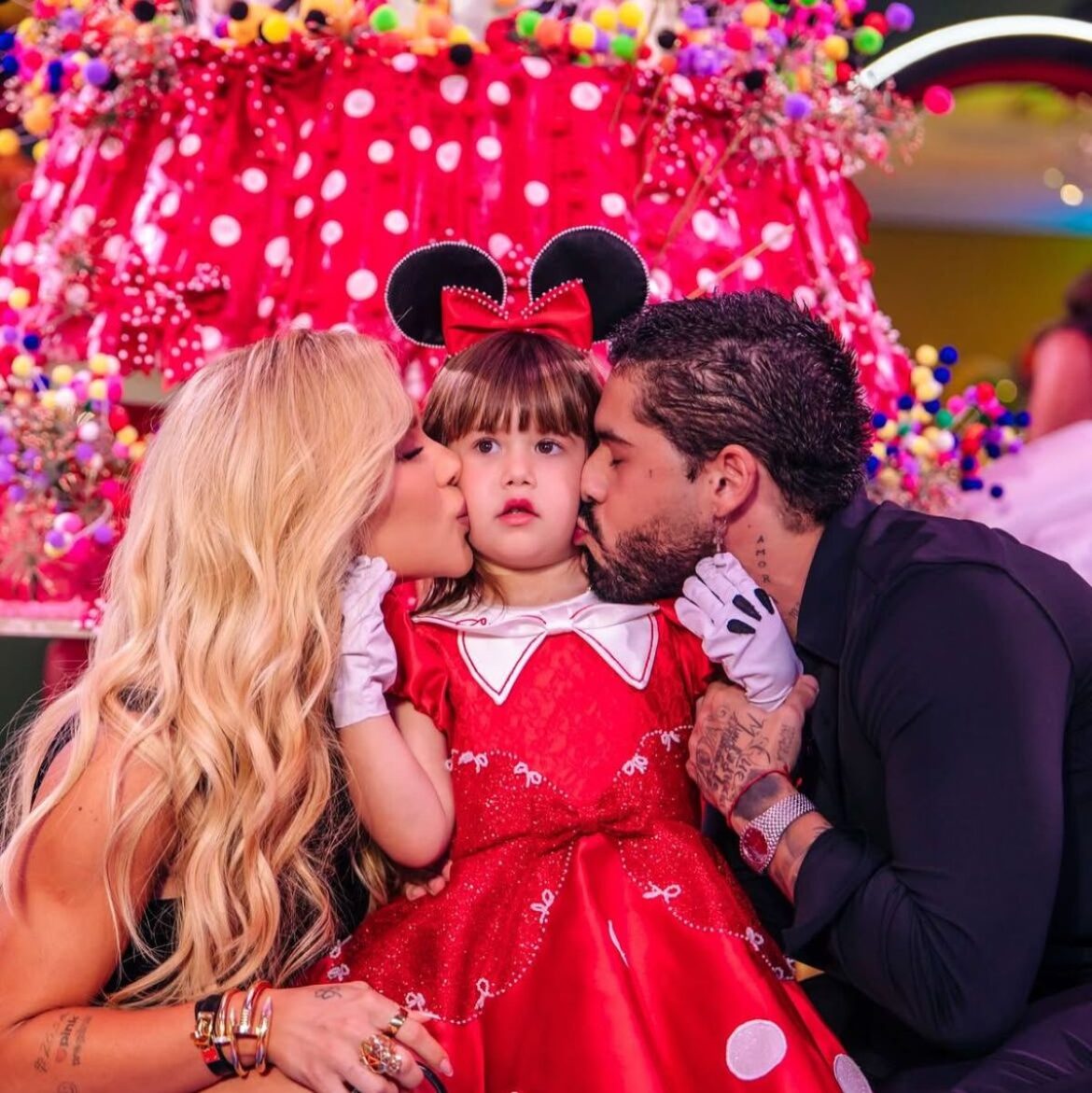 Casal beija o rosto de uma criança fantasiada em festa de aniversário com decoração vermelha