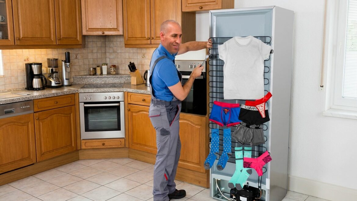 Homem sorrindo pendura camiseta, cuecas e meias no lado traseiro aberto de uma geladeira em cozinha clara