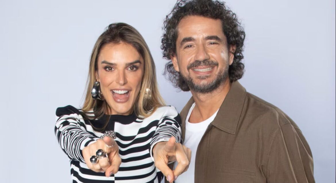 Mulher de blusa listrada e homem de blazer sorrindo e apontando para a câmera