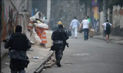 Nordeste concentra as 10 cidades mais violentas do país em 2025, revela Anuário de Segurança Pública 6 Policiais armados correm por rua de favela com moradores ao fundo, cenário urbano degradado